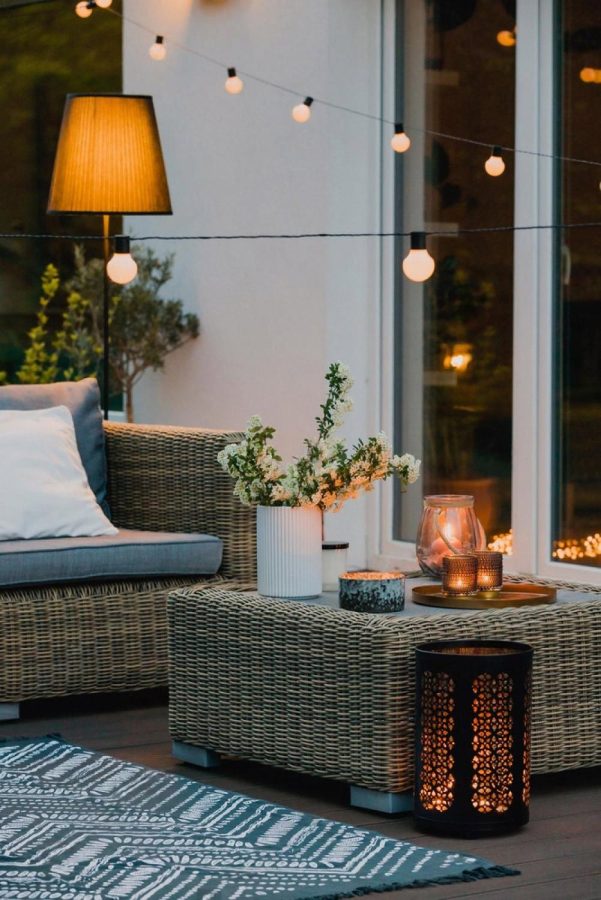Cozy outdoor patio setup at dusk with warm lighting, wicker seating and lanterns, similar to a UAE winter event lounge