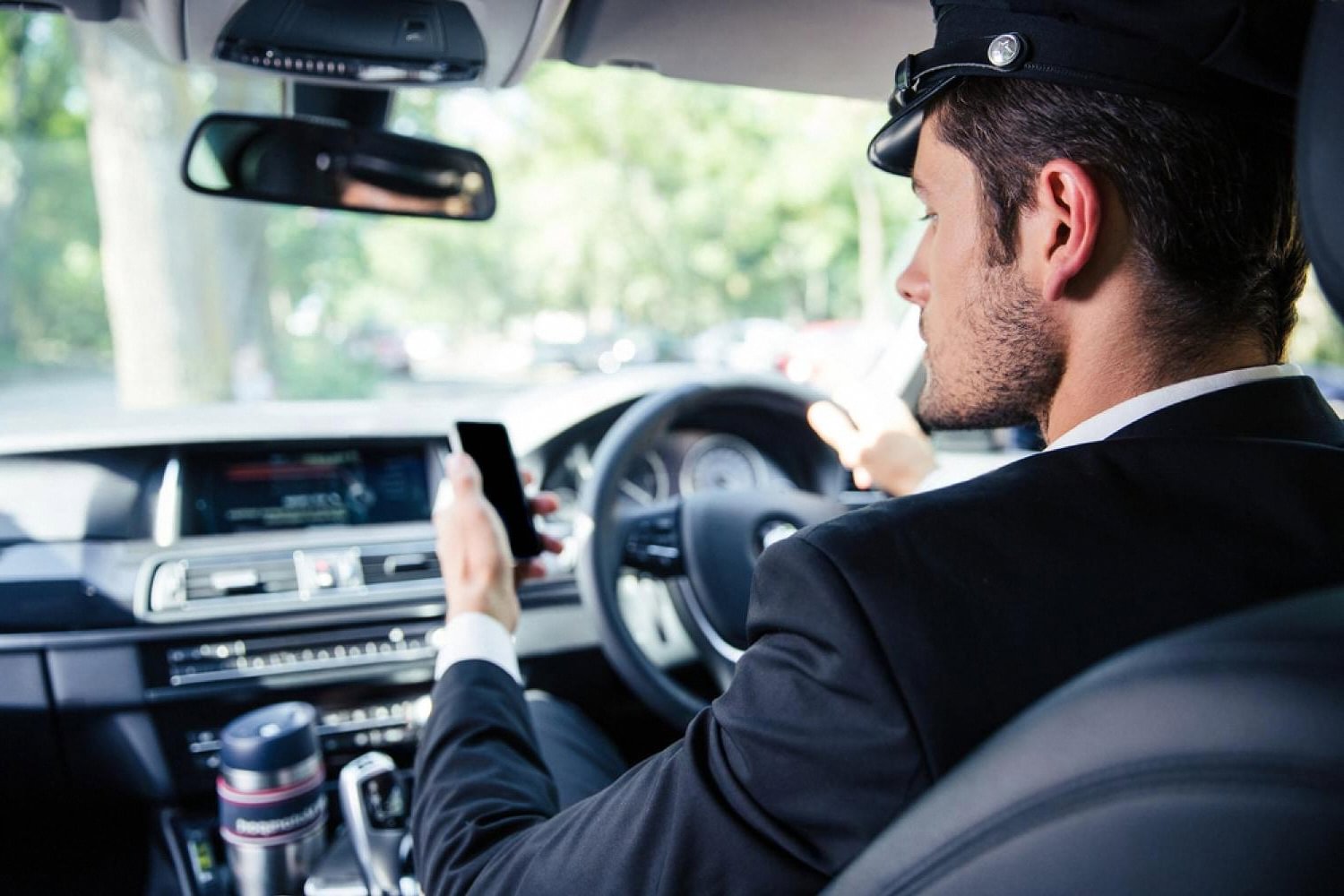 Professional chauffeur in uniform checking a phone at the wheel during a Dubai commute